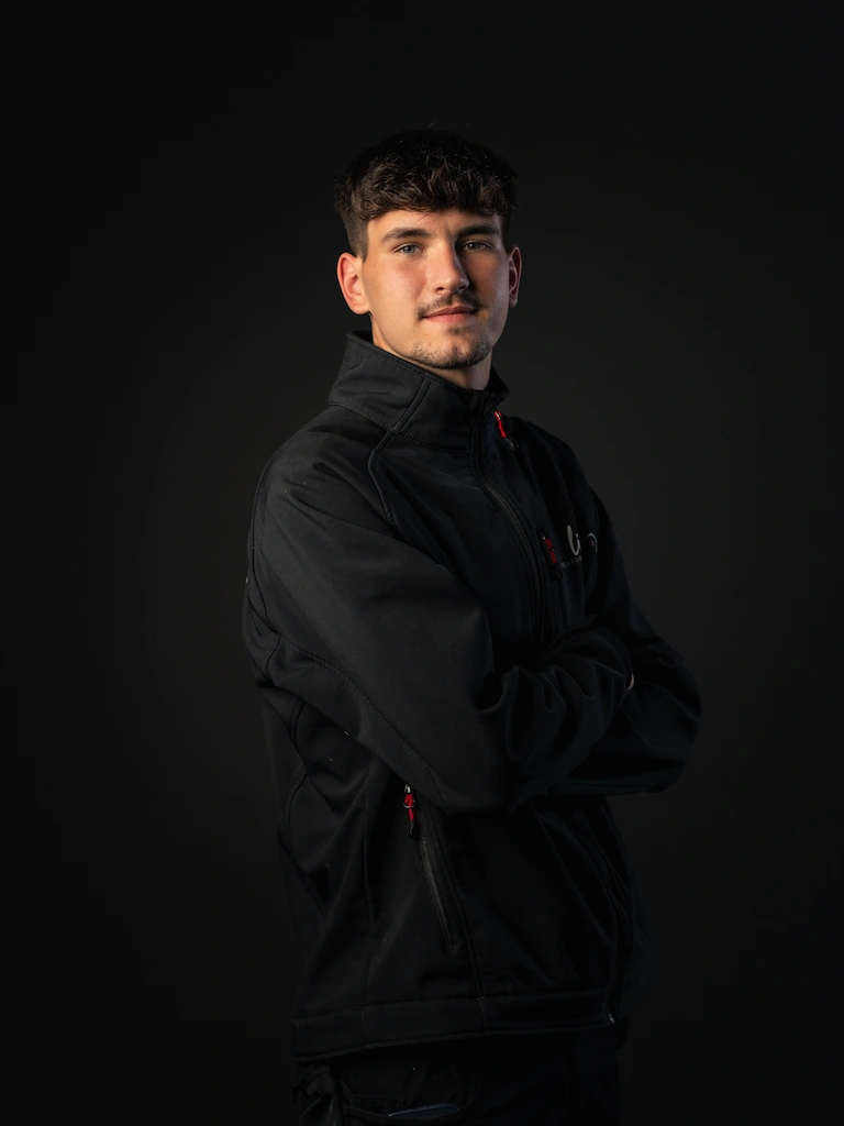 Mitarbeiter Niclas Pauly in einer Schwarzen Jacke posiert für ein Teamfoto mit verschränkten Armen.